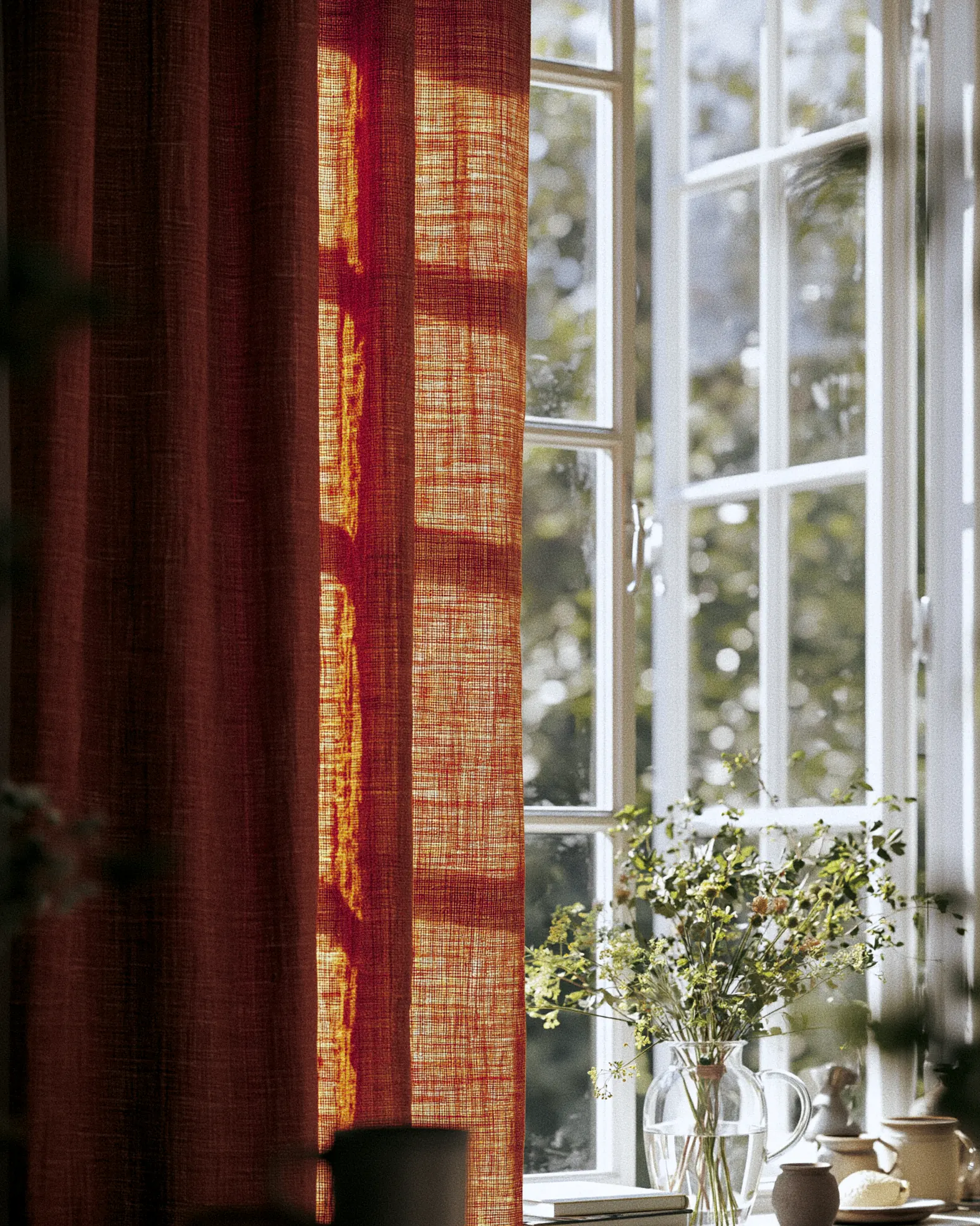 Rust-coloured open-weave curtain cloth lit from behind beside a white window.