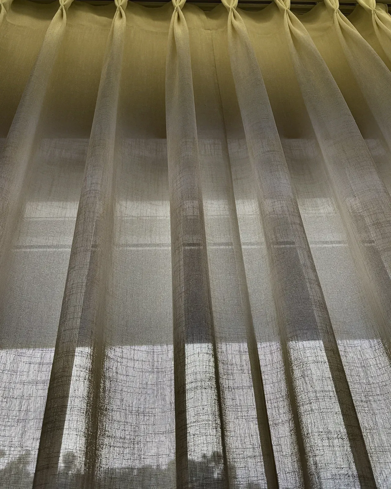 The pinch-pleat heading of a sheer, seen from below against the light.