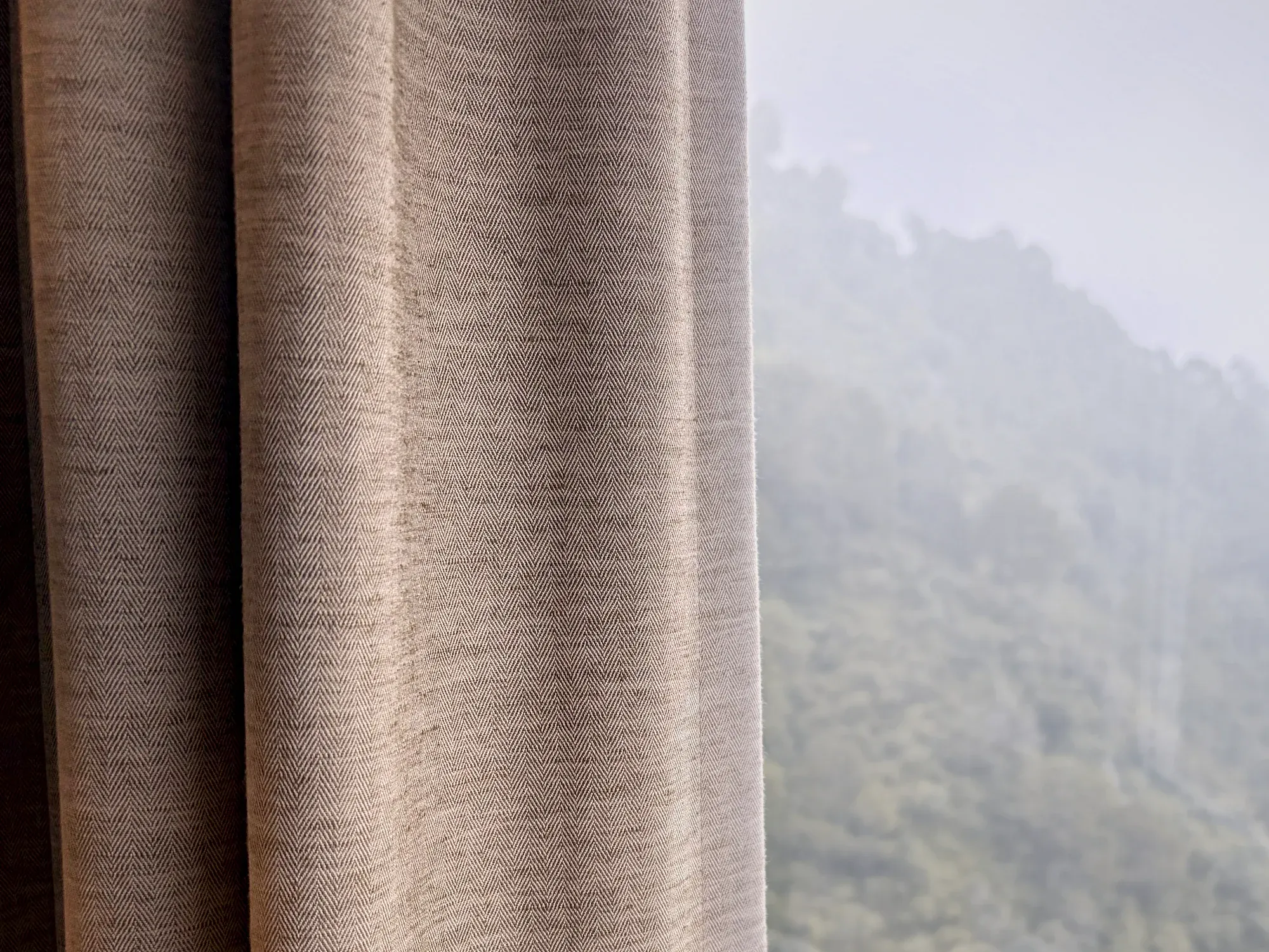 A herringbone curtain falling in fold beside a misted valley window.